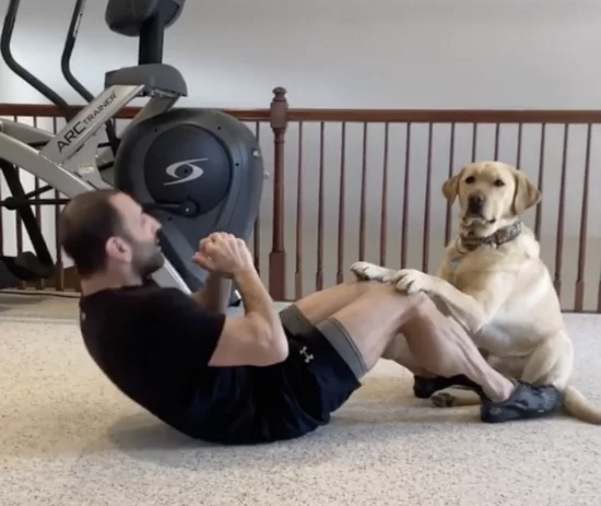 Man doing a sit-up with a dog holding his knees